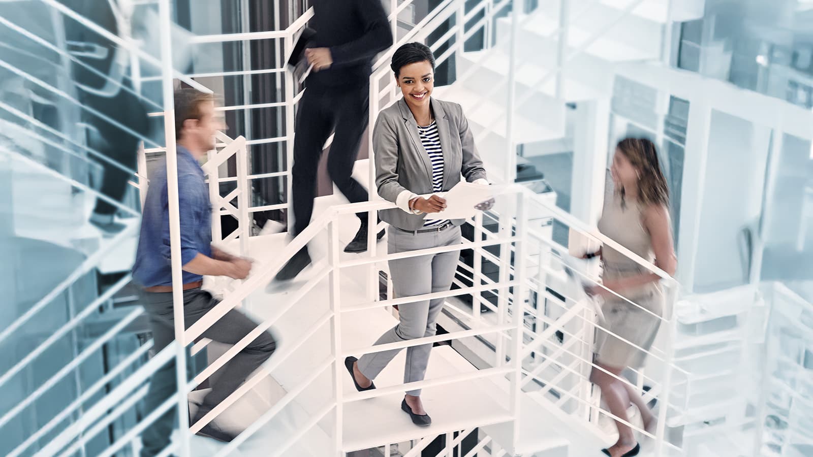 Young professional woman standing on in the middle of a stairway with colleagues ascending and descending around her.