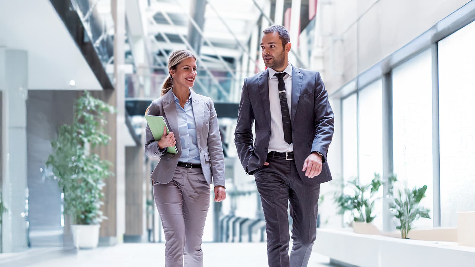 Two business professionals in conversation walking down modern building hallway.