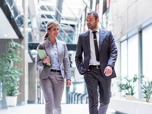 Two business professionals in conversation walking down modern building hallway.