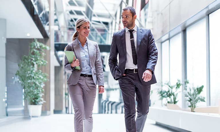 Two business professionals in conversation walking down modern building hallway.