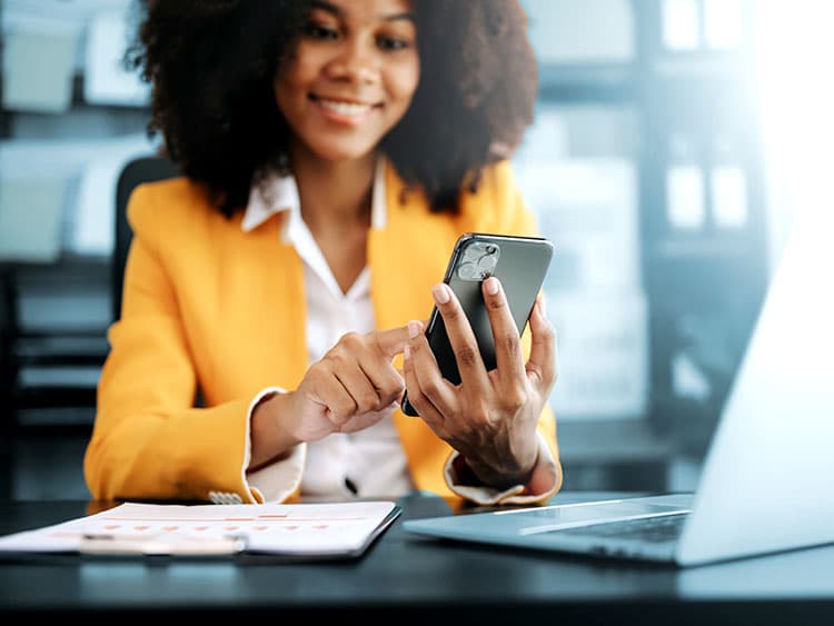 Young African businesswoman seated by her work desk using mobile phone.