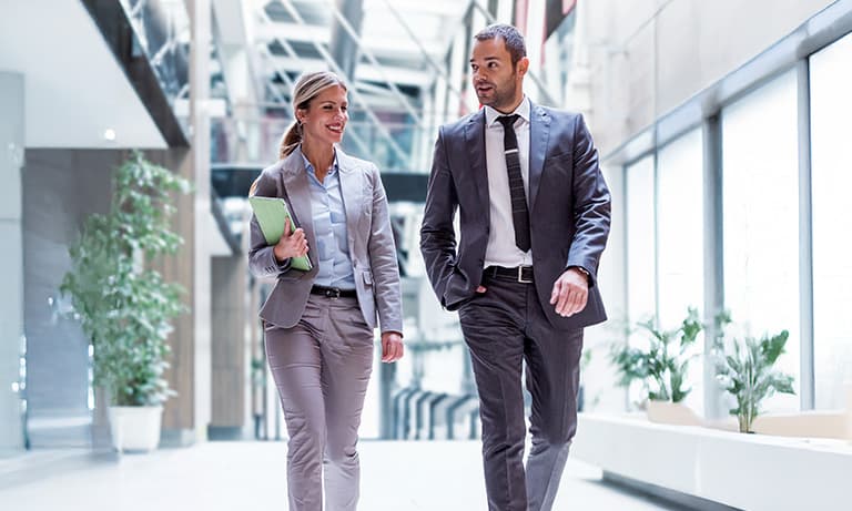Two business professionals in conversation walking down modern building hallway. Two business professionals in conversation walking down modern building hallway.